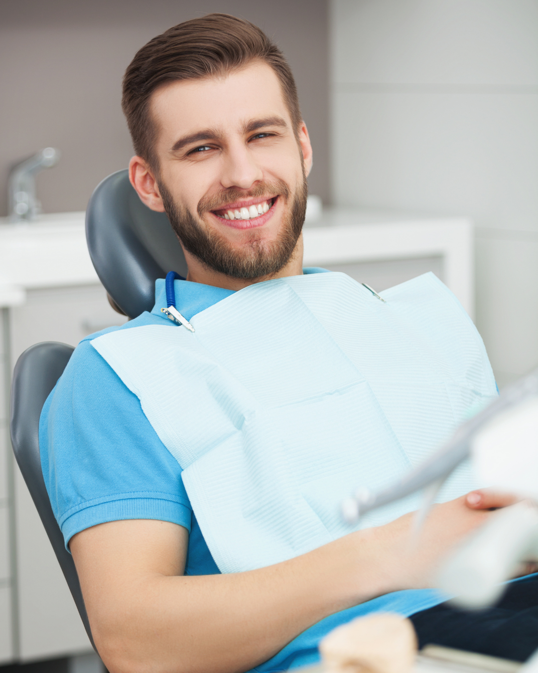 Smiling man wearing a blue shirt and dental bib waits in a dental exam chair.