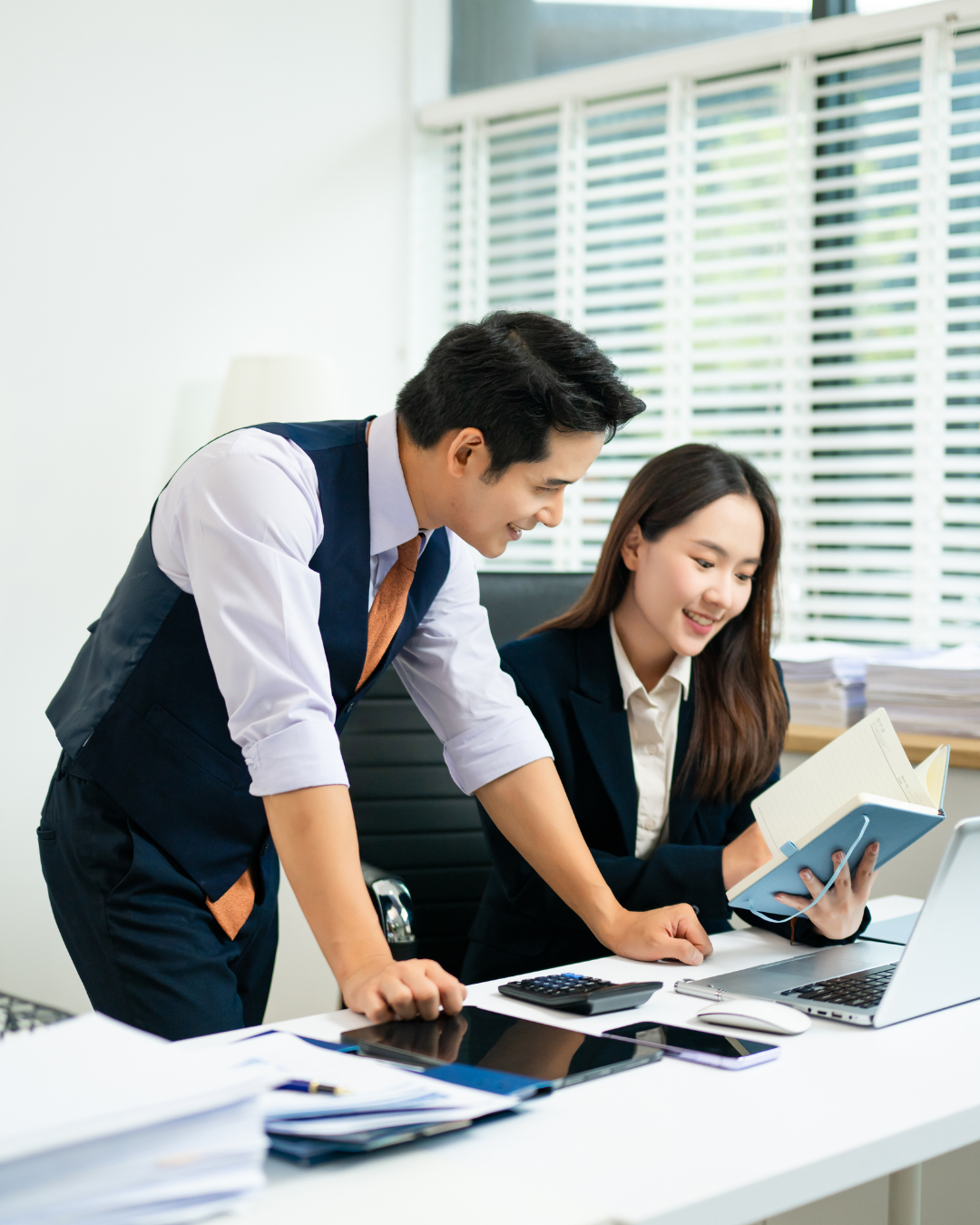 Busy man and woman lean over a desk in an office building.