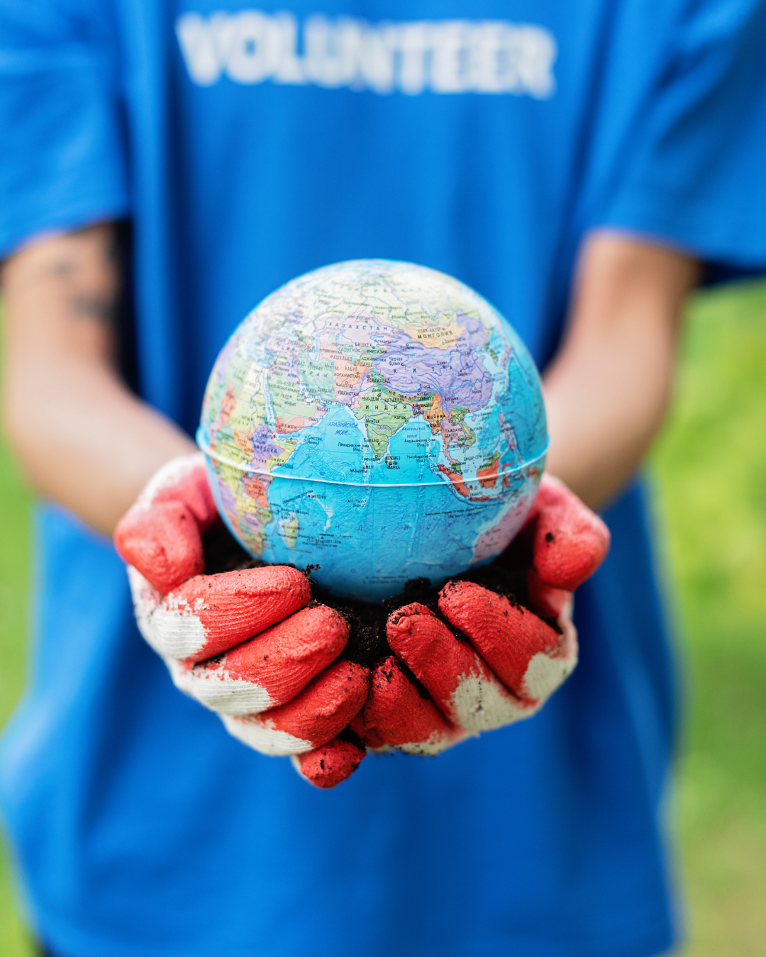 A volunteer wearing a blue shirt and red gloves holds a globe in their hands.